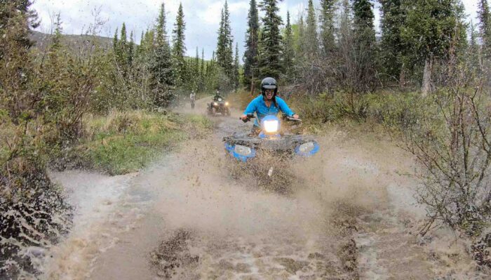 ATV rider splashing through a muddy trail during an adventurous Alaska tour