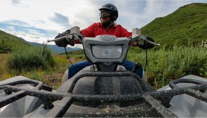 Solo ATV rider tearing through a mud-covered trail on an Alaskan wilderness tour