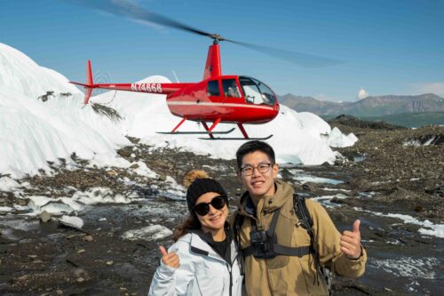 Helicopter parked on a glacier as passengers explore during an Alaskan tour.