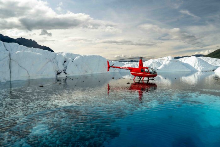 Helicopter parked in a vibrant blue meltwater pool on a glacier during an Alaskan adventure tour.