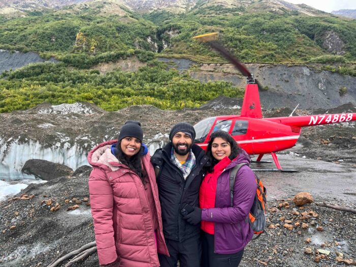 Couple posing in front of a helicopter on a glacier, enjoying an Alaskan adventure.