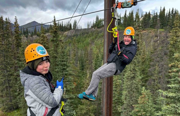 Zipline rider still hanging mid-air, laughing off a close finish during an exciting Alaskan zipline race.