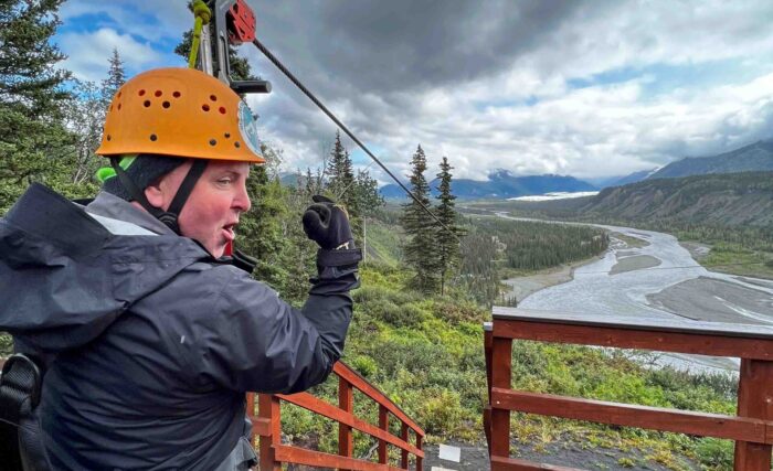 A man standing at the starting platform, ready to launch on a thrilling zipline adventure in Alaska.