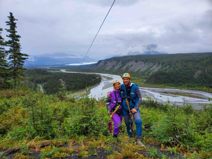 A couple posing triumphantly before completing an epic zipline ride in the Alaskan outdoors