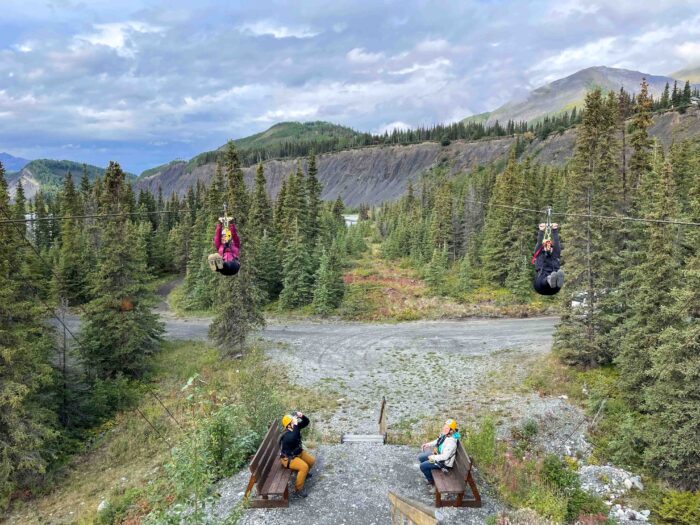 Two zipline riders coming in neck-and-neck for an exciting close finish against the backdrop of Alaska's stunning scenery.